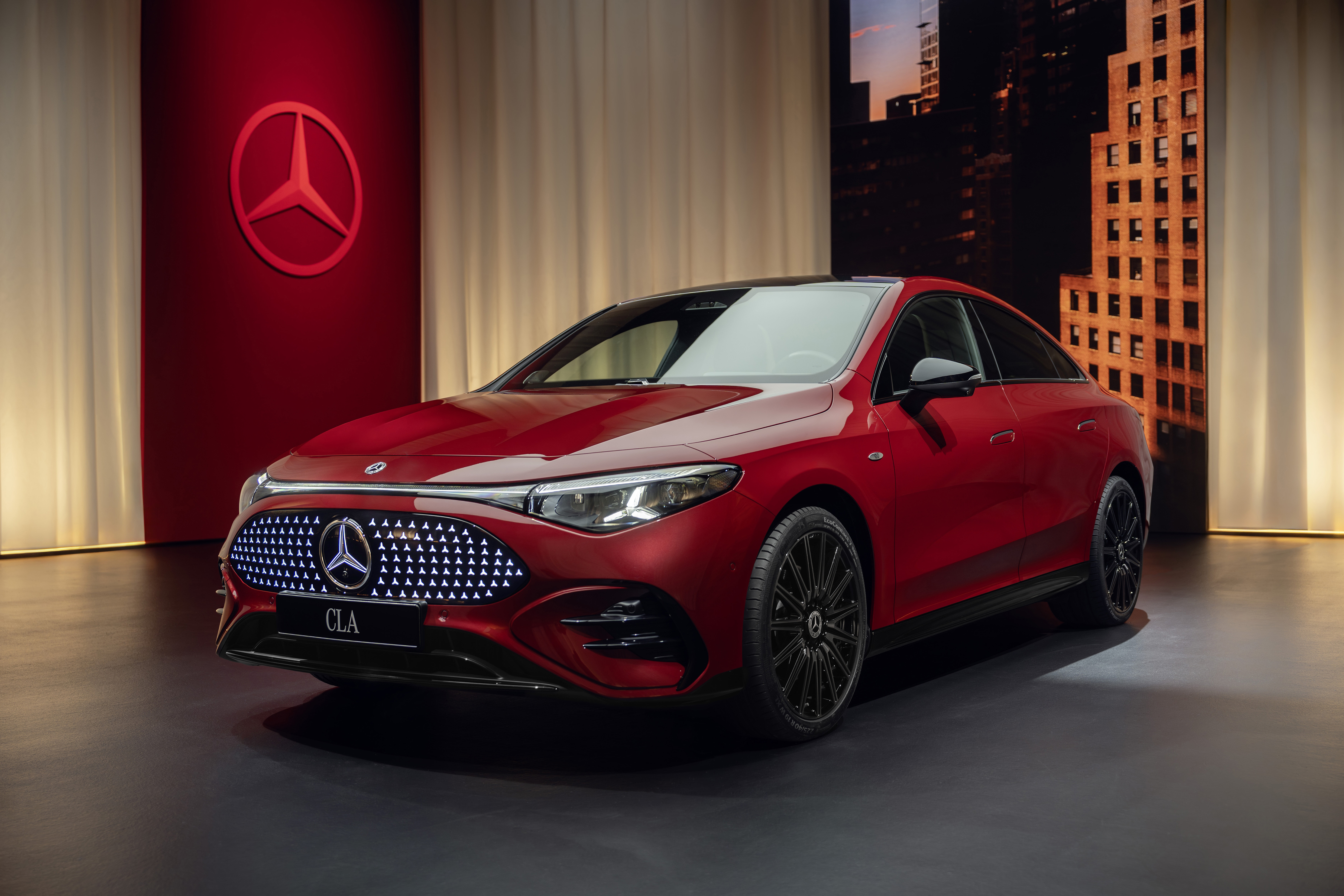 „Nový Mercedes-Benz CLA 2025 ve verzi 250+ EQ – přední pohled na osvětlovaný panel s LED hvězdami a charakteristickými světlomety ve tvaru hvězdy. Moderní elektrický design a futuristická silueta coupé.“